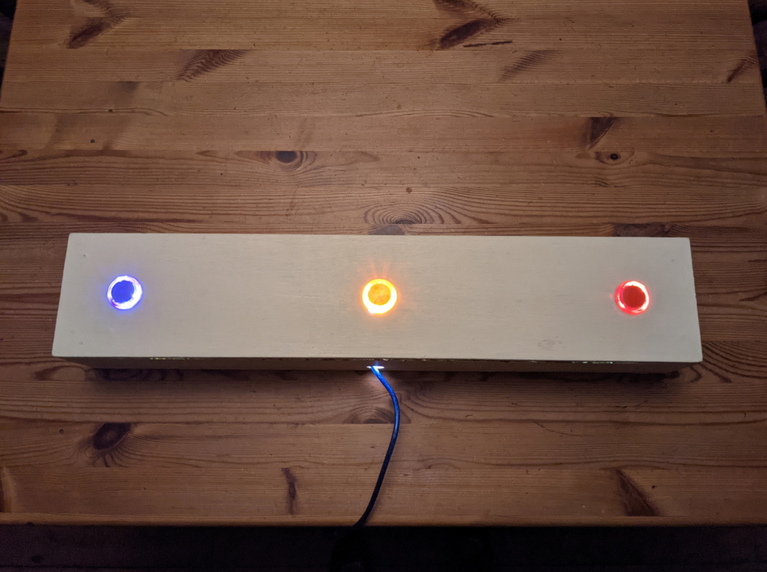 A photo of a very wide wooden box with 3 arcade buttons spaced along it.